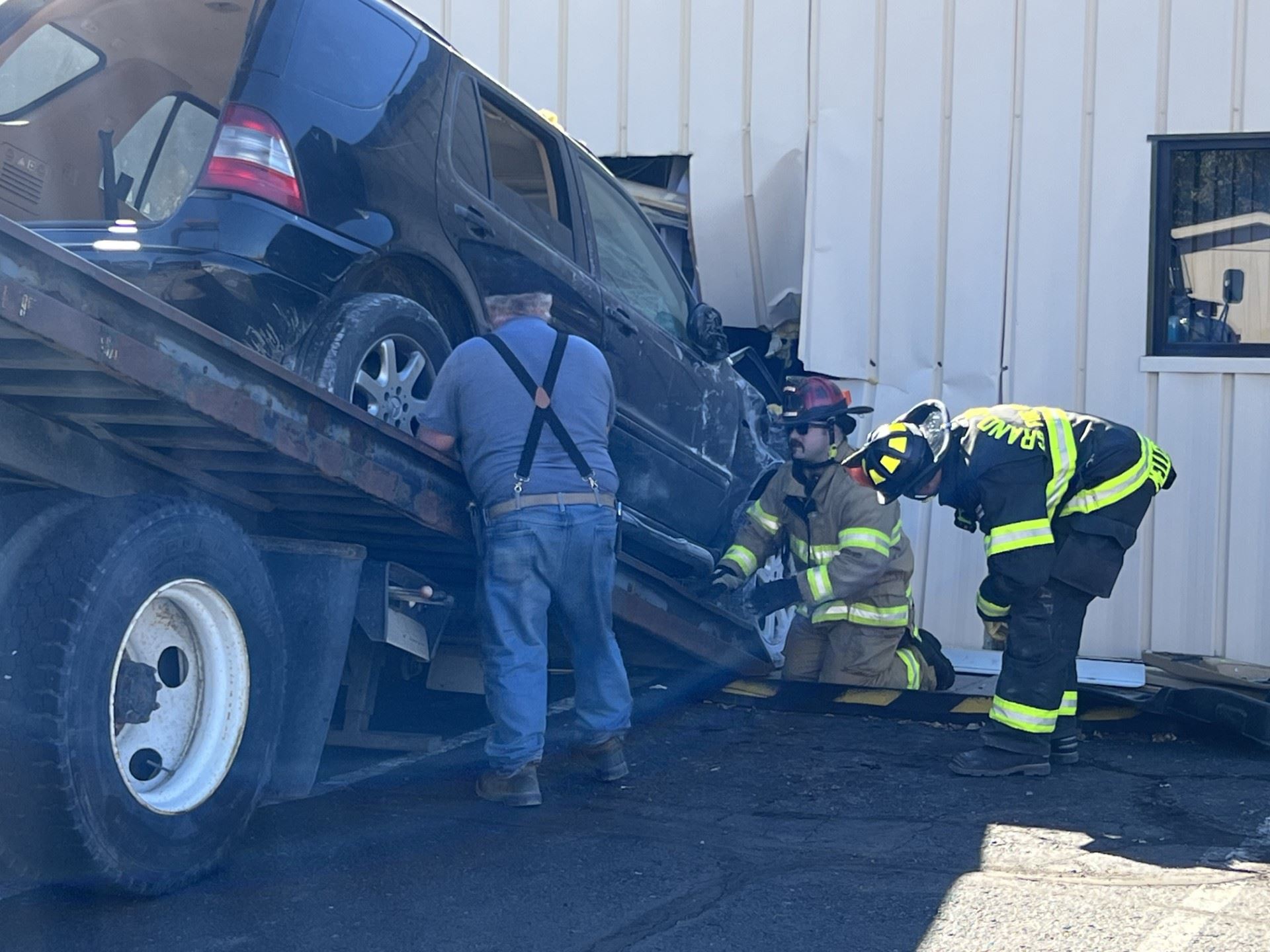 firefighters assisting tow truck with removal of vehicle from building