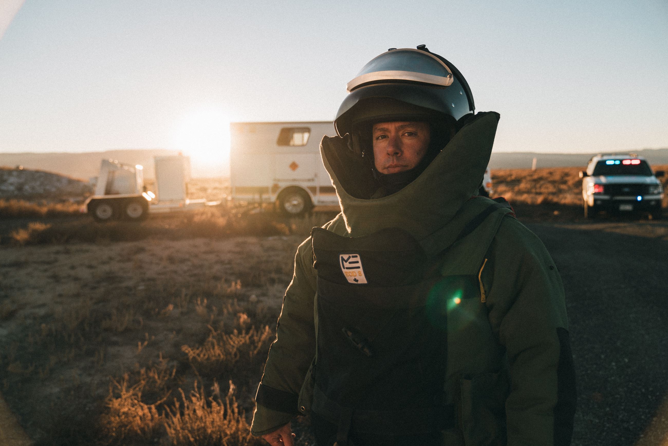 Member of the Bomb Unit posing for a photo with Bomb vehicles in background.